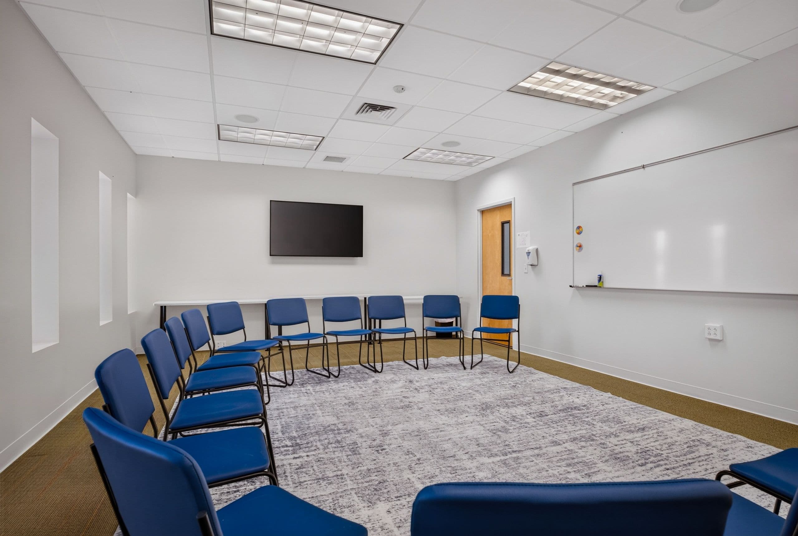 A second group room, with blue chairs in a circle facing a whiteboard and screen